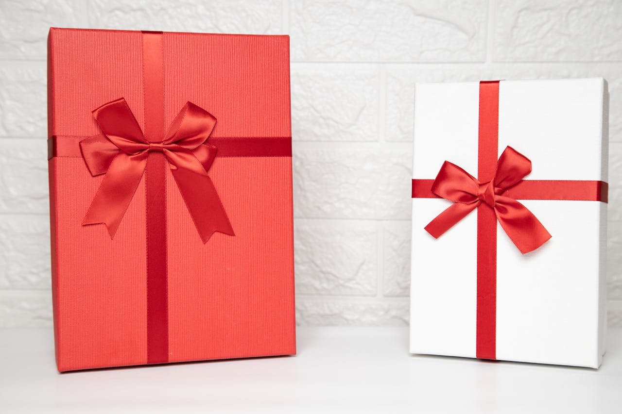 Two stylish gift boxes with red ribbons on a white indoor background, perfect for celebrations.