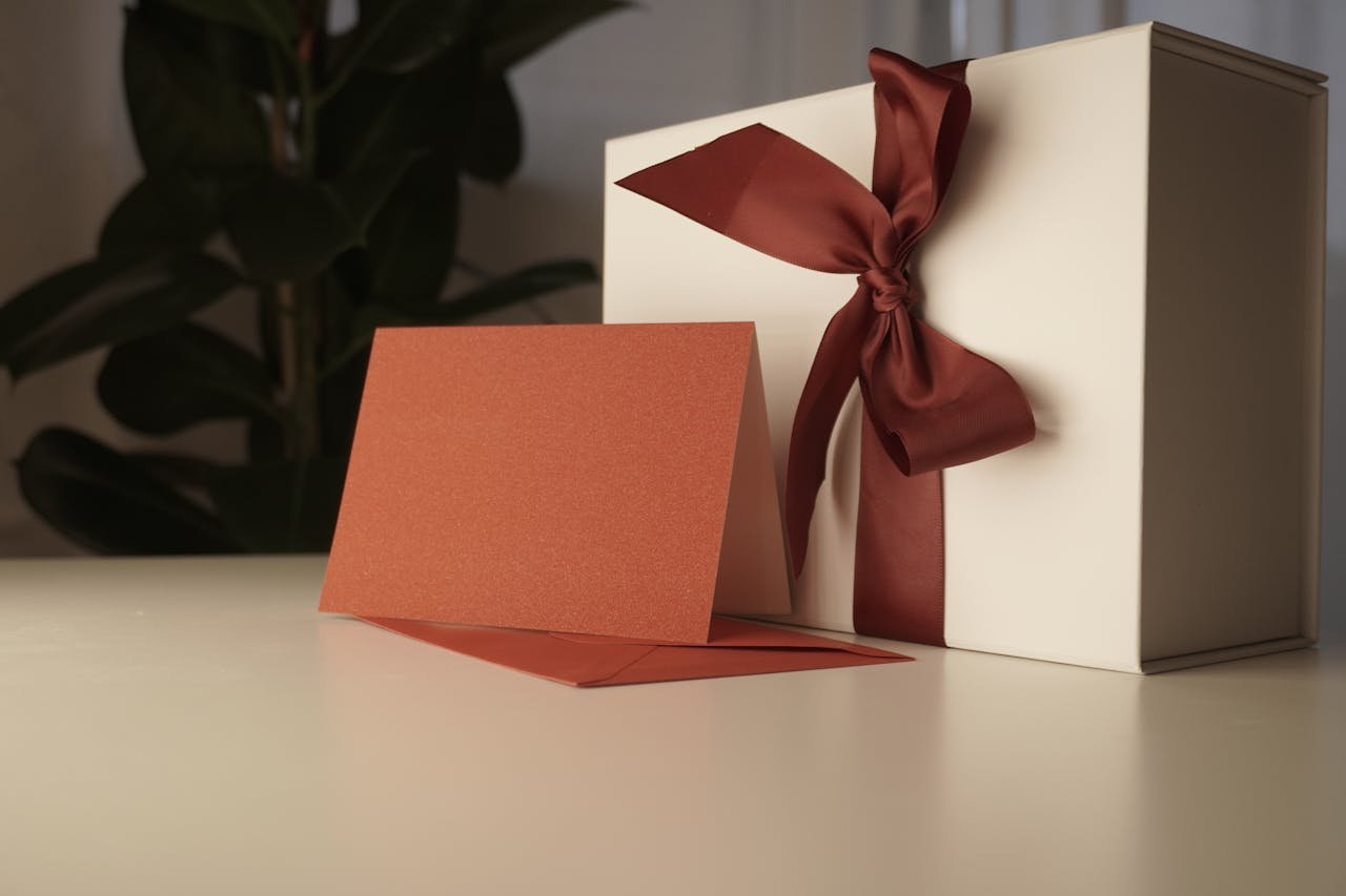 White gift box with red ribbon and greeting card on a table indoors.