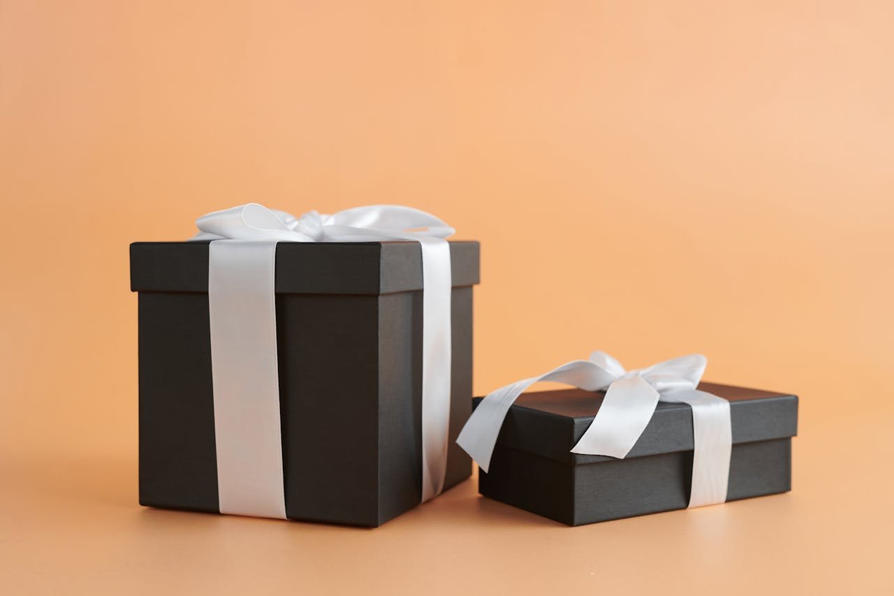 Two black gift boxes with white ribbons on a beige background, perfect for celebrations.
