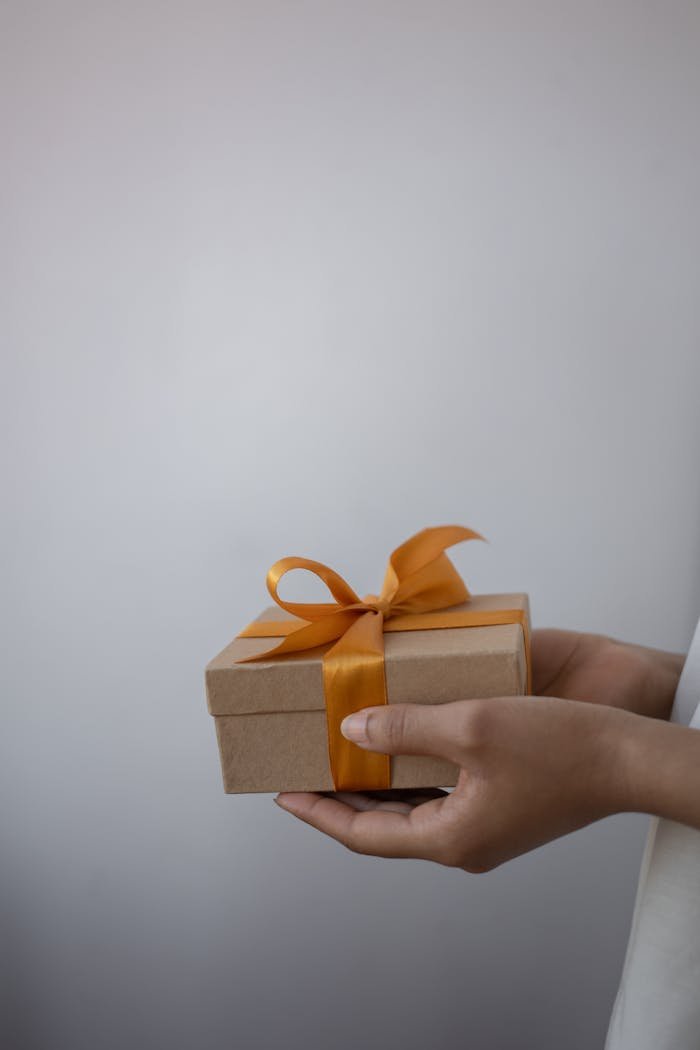 A close-up of hands holding a gift box decorated with an orange ribbon bow.